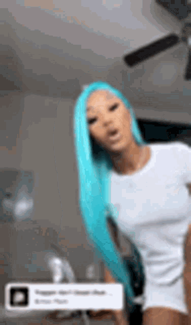 a woman with long blue hair is wearing a white t-shirt and standing in a room .