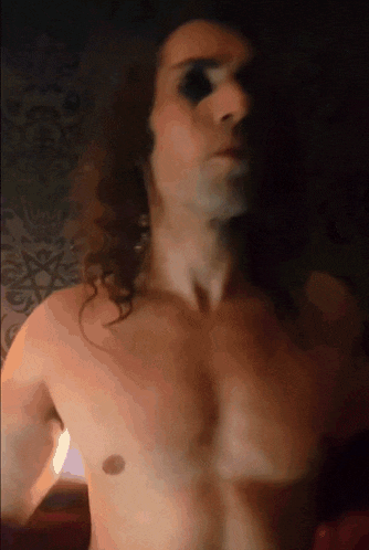 a shirtless man with long hair has a black eye on his forehead