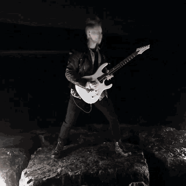 a man playing a guitar in the dark on a rock