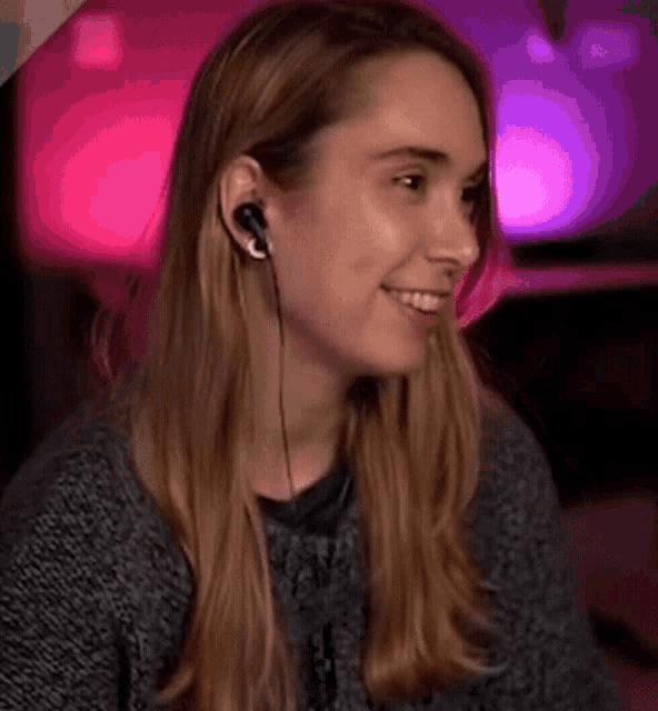 a woman wearing headphones and a sweater is smiling and looking to the side .