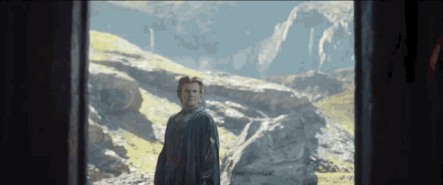 a man in a black robe stands in front of a mountain range