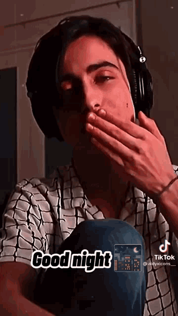 a young man wearing headphones is covering his mouth with his hand and says good night