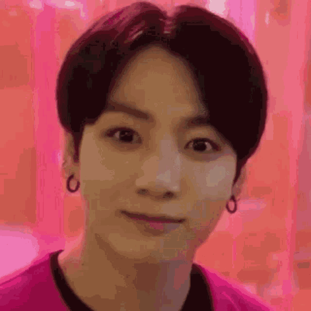 a close up of a young man wearing a pink shirt and earrings .