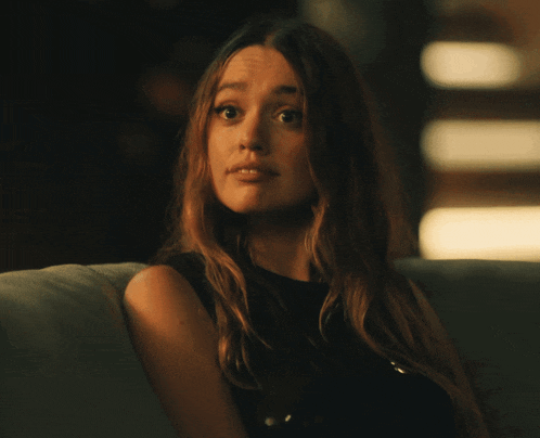 a woman with long hair is sitting on a couch and making a face