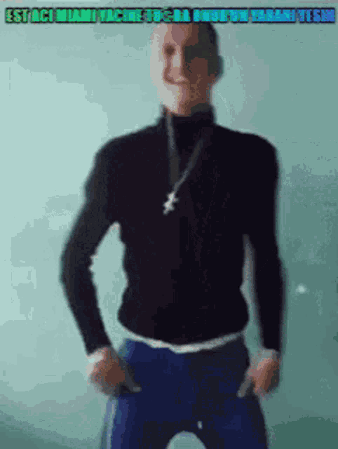 a man in a black turtleneck and blue pants is standing with his hands in his pockets