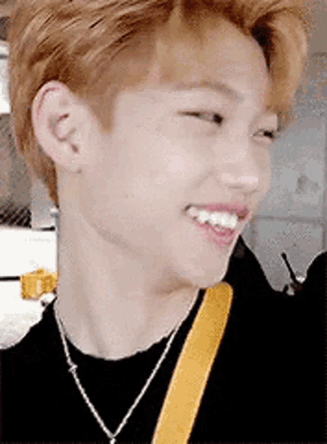 a close up of a young man wearing a black shirt and a necklace smiling .