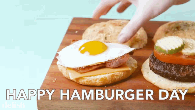 a hamburger with a fried egg and cheese is on a wooden cutting board with the words happy hamburger day above it