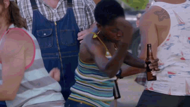 a man in overalls is holding a bottle of beer while dancing with a woman in a striped tank top .