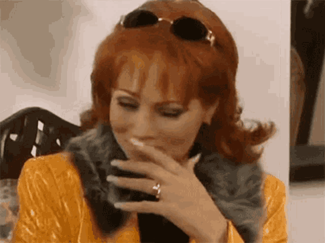 a woman with red hair is wearing sunglasses and a fur coat and covering her mouth with her hand .