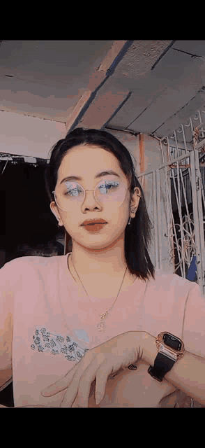 a girl wearing glasses and a pink shirt is standing in front of a fence