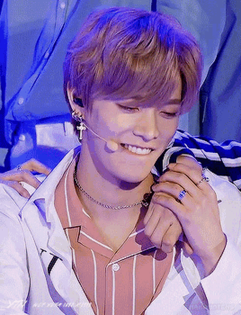 a young man wearing a striped shirt and a white jacket is smiling while wearing a microphone .
