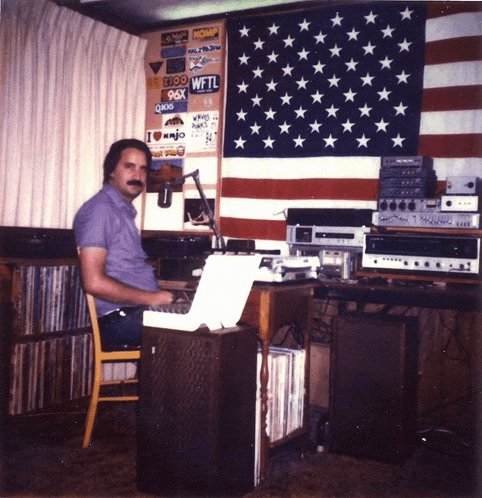 a man sits at a desk in front of an american flag with a sticker on the wall that says wfl