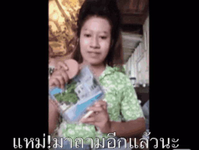 a woman in a green shirt is holding a book in her hand
