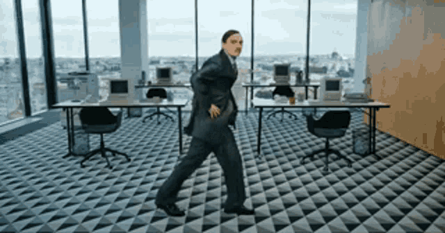 a man in a suit is walking through an office with computers on the desks