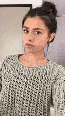a woman wearing a sweater and hoop earrings is taking a selfie .