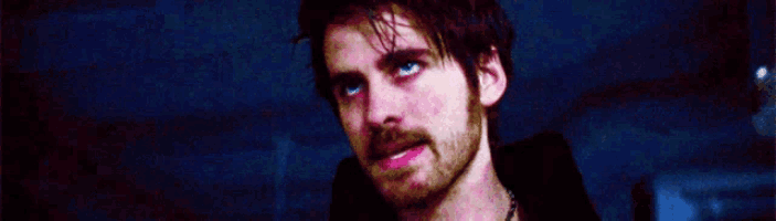 a man with a beard and blue eyes is standing in a dark room .