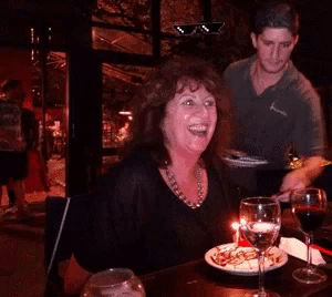 a woman sitting at a table with a plate of food and wine glasses