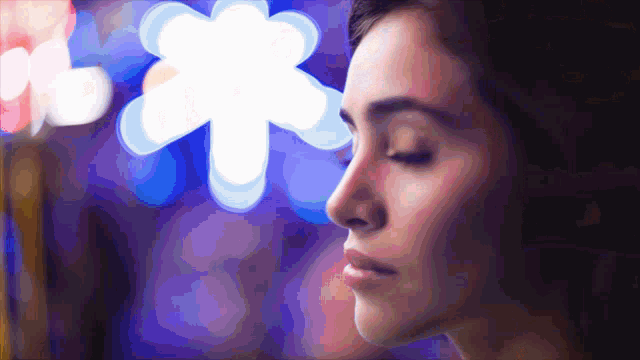 a close up of a woman 's face with her eyes closed and a flower in the background