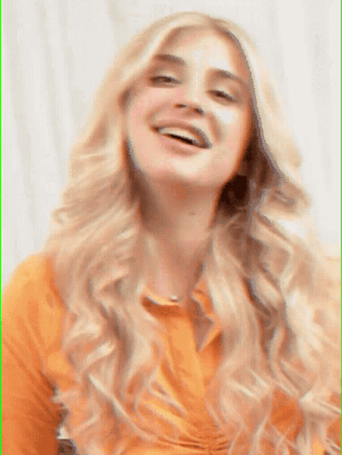 a woman with long blonde hair is smiling and wearing an orange shirt .