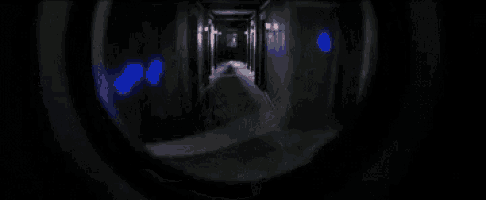 a man in a black shirt is sitting in a dark room looking up at something .