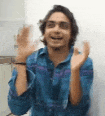 a man in a blue shirt is making a funny face while raising his hands in the air .
