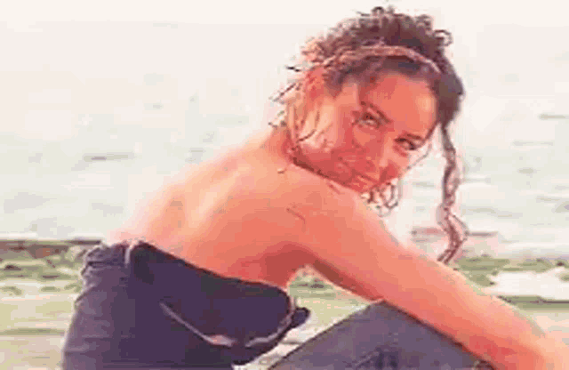 a woman in a strapless top is sitting on a rock by the ocean .