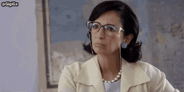 a woman wearing glasses and a pearl necklace is sitting in front of a map .