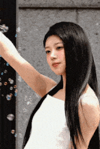 a woman with long black hair is standing in front of a wall with bubbles flying around her .