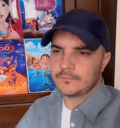 a man wearing a hat and a blue shirt is sitting in front of a wall with posters of disney movies on it .