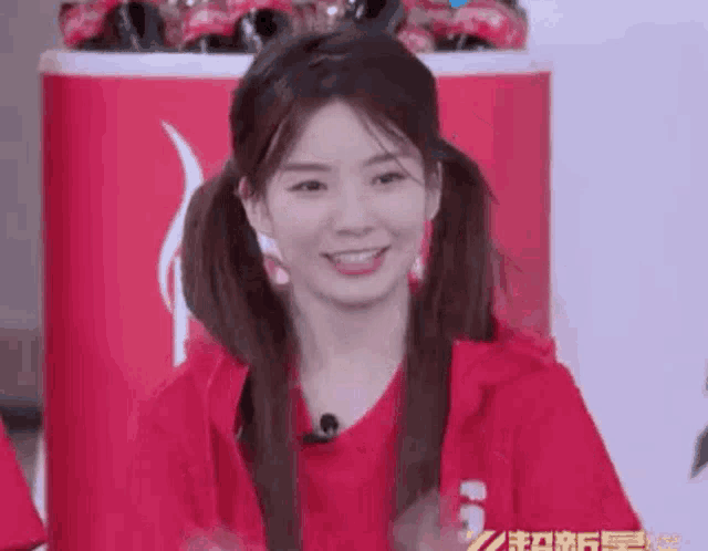 a woman with pigtails is wearing a red hoodie and smiling .