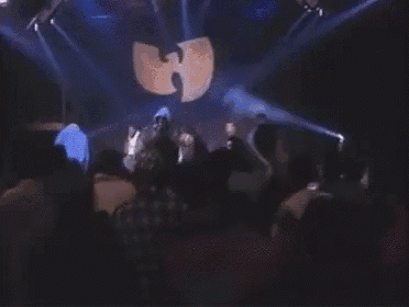 a group of people are standing in front of a stage with a huge wu tang logo on it