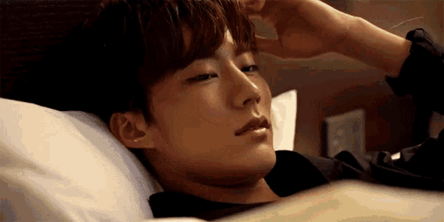 a young man laying in a bed with his hand on his forehead
