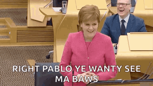 a woman in a pink jacket is giving a speech in front of a microphone in a parliament .