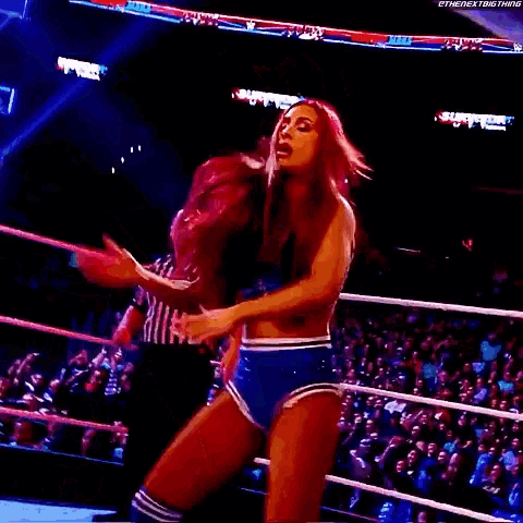 a female wrestler with the number 5 on her shorts is standing in a wrestling ring