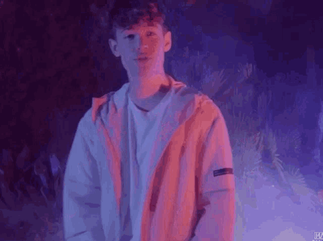 a young man is standing in a dark room with a purple background .