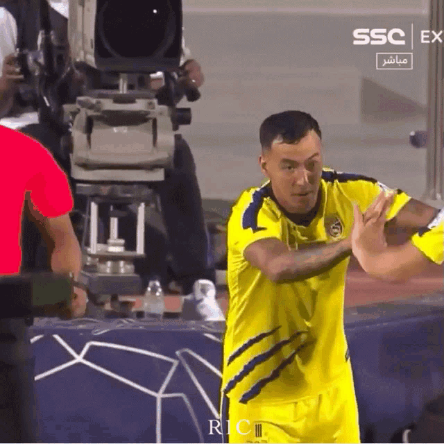 a soccer player in a yellow jersey stands in front of a camera with the words ssc ex on the bottom