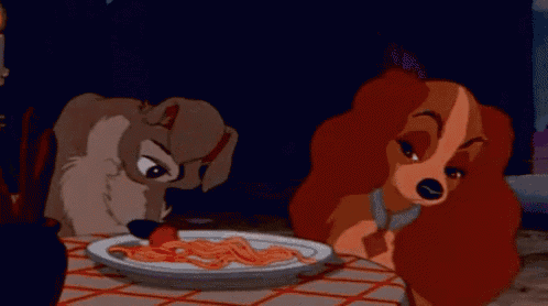 a dog and a woman are sitting at a table eating spaghetti .