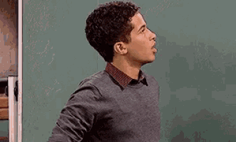 a man is covering his mouth with his hand in front of a blackboard .