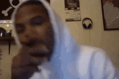 a man wearing a white hoodie is sitting in a room with headphones on the wall .