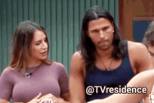 a man with long hair is standing next to a woman in a purple shirt with the words @tvresidence written below him .