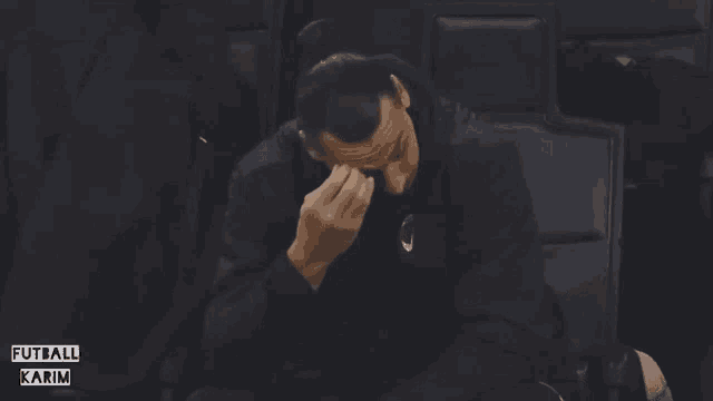 a man is covering his face with his hand and the words futball karim are on the bottom right