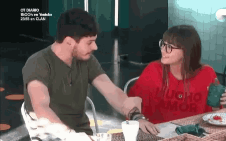 a man and a woman are sitting at a table and the man is wearing a shirt that says mucho amor