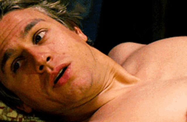 a man without a shirt is laying down with his mouth open