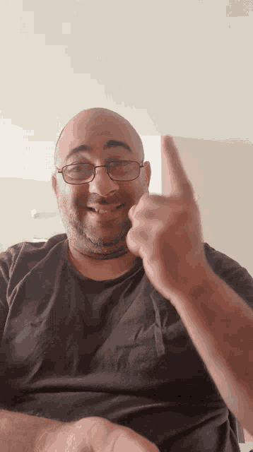 a man wearing glasses and a black shirt is giving a thumbs up