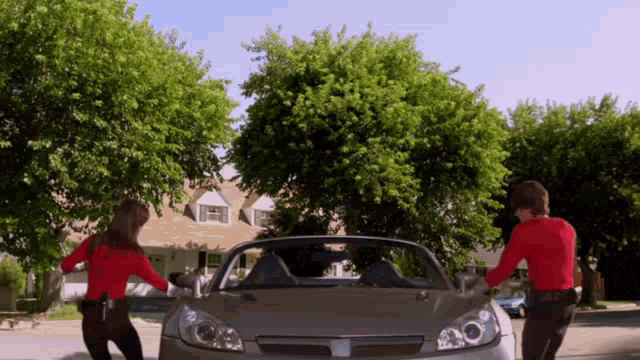 a man and a woman are standing in front of a convertible car