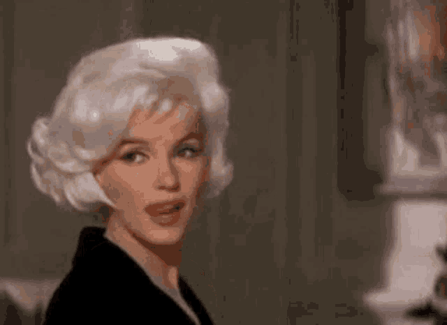 a woman with blonde hair and a black dress is standing in front of a lamp .