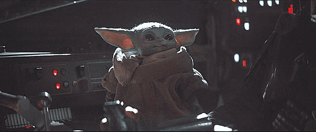 a baby yoda is sitting in a dark room with a red light behind him