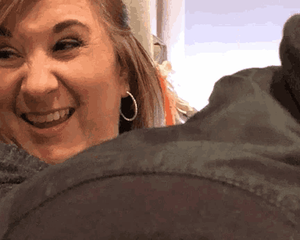 a woman wearing hoop earrings is smiling while holding a jacket .