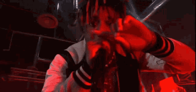 a man with dreadlocks is singing into a microphone in a dark room with red lights .