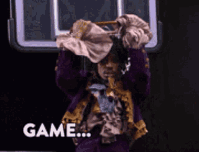 a person in a purple and gold outfit is holding a pink shirt over their head and the word game is on the bottom